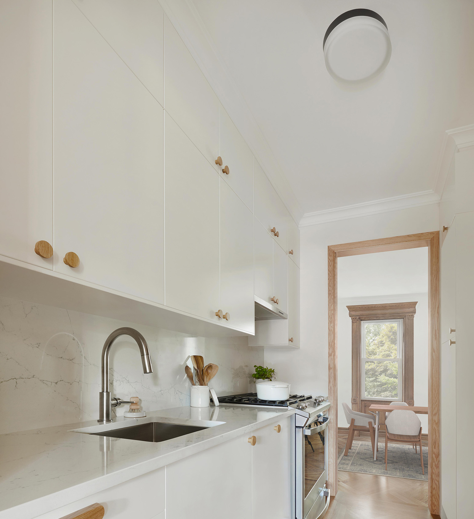 Flush mount ceiling light, white kitchen cabinets, wooden hardware and wooden floor kitchen.