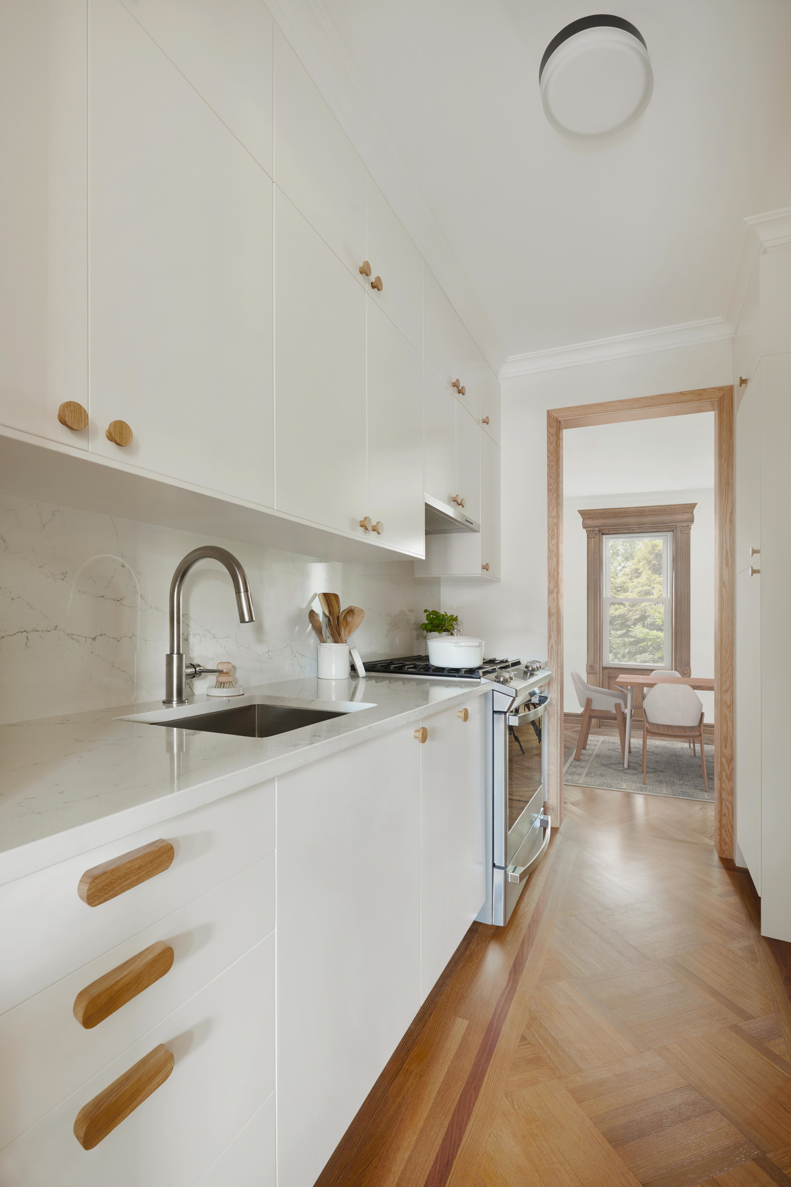 Flush mount ceiling light, white kitchen cabinets, wooden hardware and wooden floor kitchen.