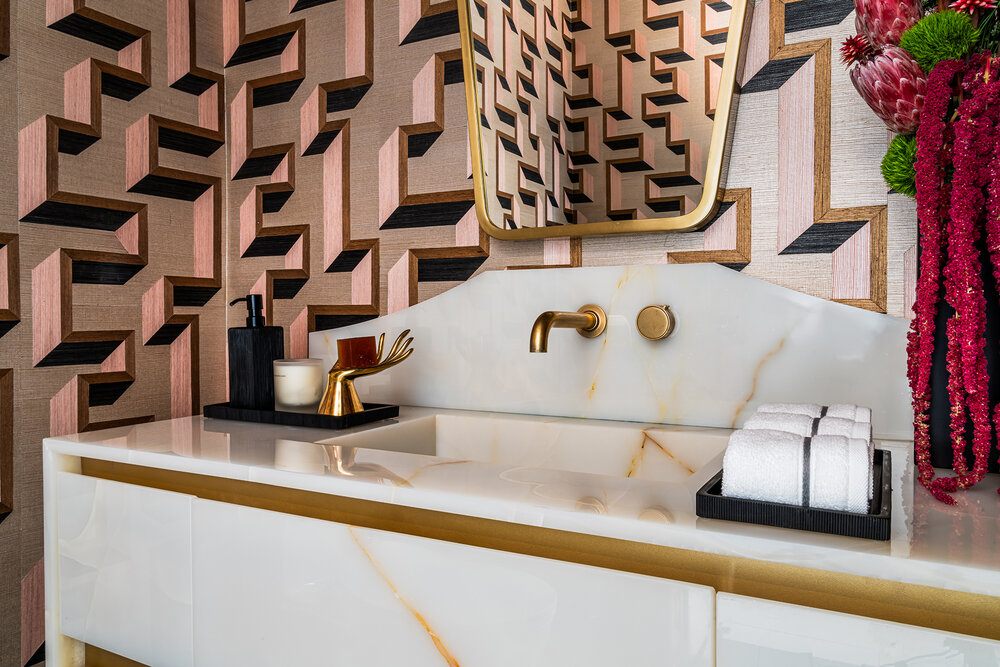 Modern bathroom design with geometric wallpaper, white marble vanity, gold faucet, and mirror. Stylish powder room featuring luxury finishes, pink and black 3D wall pattern, and elegant countertop decor with towels and flowers.