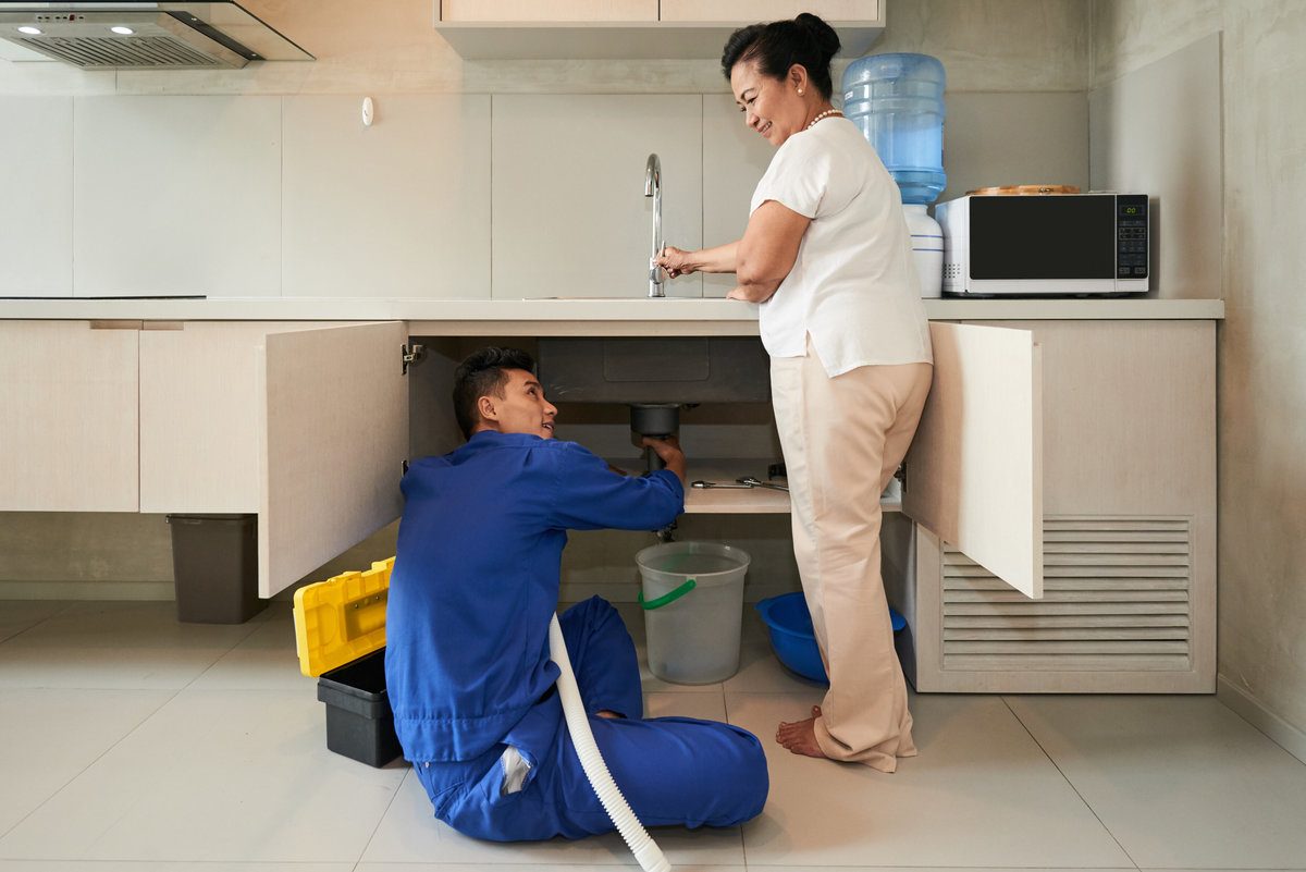 Plumber Unclogging Kitchen Sink with Homeowner Testing Tap