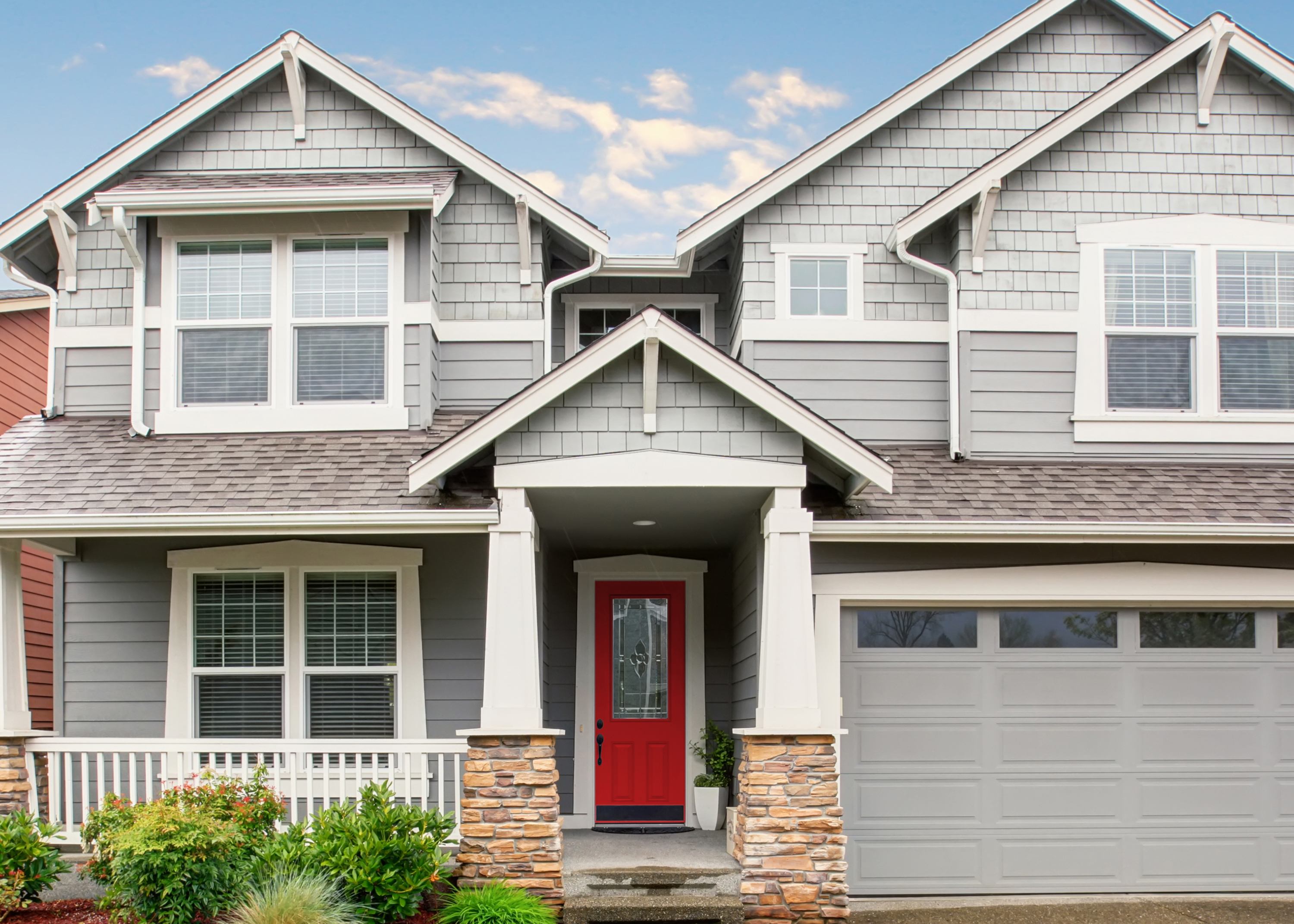 A big gray house with a garage, red front door and white trim.