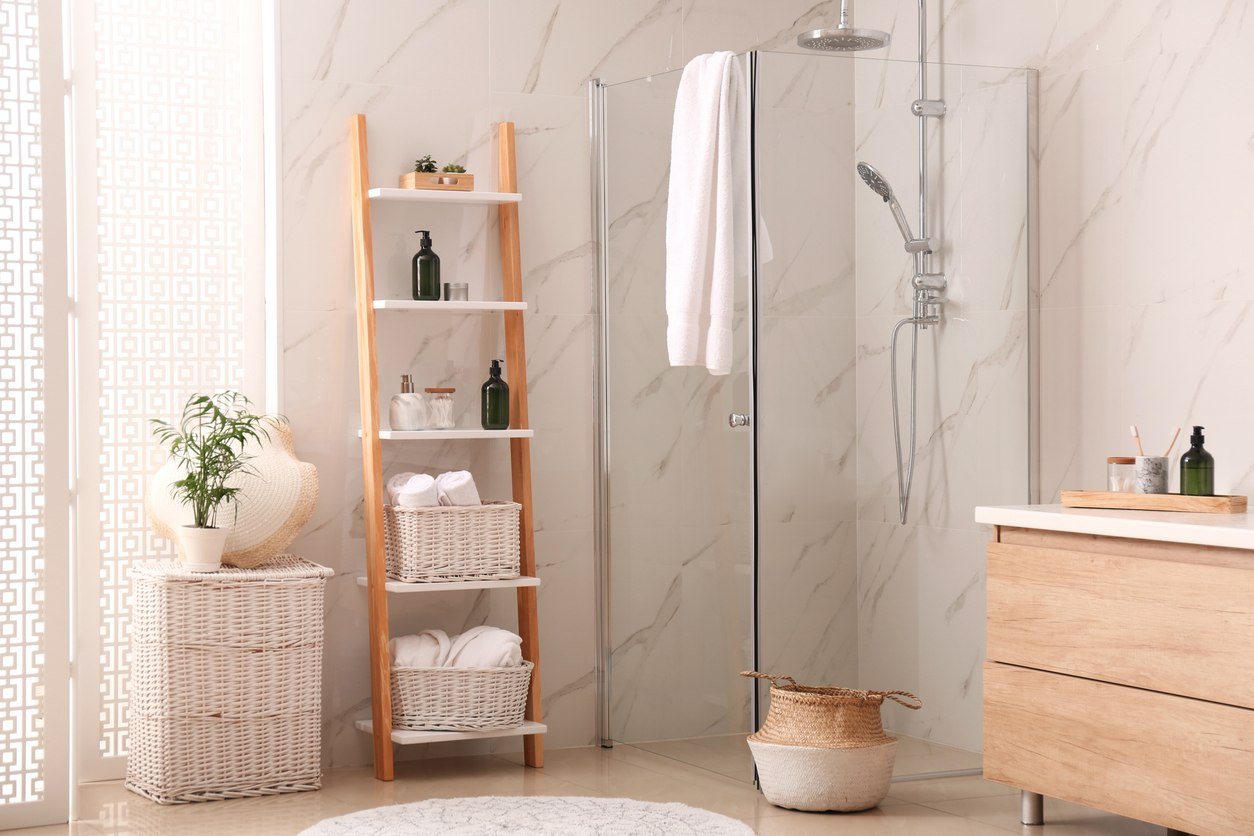 A modern bathroom with marble tiles, wooden vanity, modern shelving and a frameless glass shower.