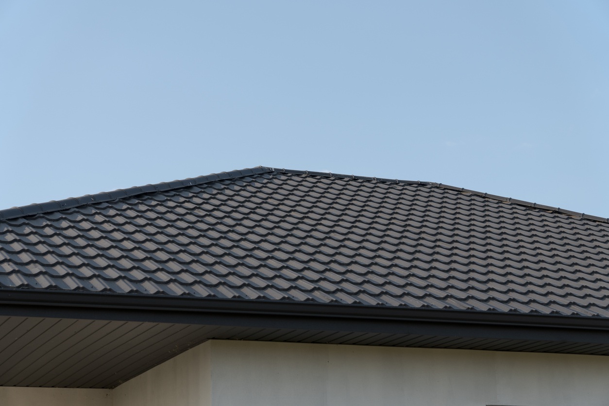 A dark metal shallow-sloped hip roof under the clear blue sky.